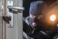 Masked burglar holding flashlight while trying to break window l Royalty Free Stock Photo