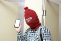 Masked burglar holding and showing mobile smart phone on his hands in toilet. Dangerous social crime concept.