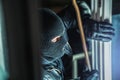 Masked burglar with torch and crowbar breaking and entering into a house