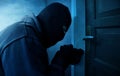 Masked burglar using lock picker to open locked door