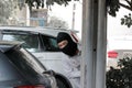 Masked burglar wearing a balaclava and sneaking behind concrete pole before the burglary in car park. Crime concept Royalty Free Stock Photo