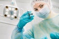 A masked dentist holds an injection syringe for a patient in the office