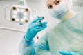 A masked dentist holds an injection syringe for a patient in the office