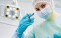 A masked dentist holds an injection syringe for a patient in the office