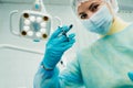 A masked dentist holds an injection syringe for a patient in the office