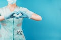 A masked doctor with a stethoscope shows a heart sign on his chest with his hands. The concept of health and care of patients,