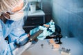 A masked and gloved dental technician works on a prosthetic tooth in his lab