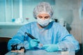 A masked and gloved dental technician works on a prosthetic tooth in his lab