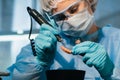 A masked and gloved dental technician works on a prosthetic tooth in his lab