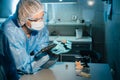 A masked and gloved dental technician works on a prosthetic tooth in his lab