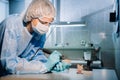 A masked and gloved dental technician works on a prosthetic tooth in his lab