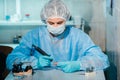 A masked and gloved dental technician works on a prosthetic tooth in his lab