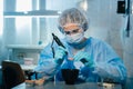 A masked and gloved dental technician works on a prosthetic tooth in his lab