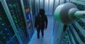 Masked hacker with his laptop waking through server rows