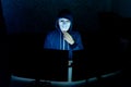 Masked hacker under hood using computer to hack into system and trying to commit computer crime.
