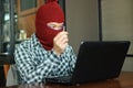 Masked hacker wearing a balaclava holding fake key between stealing data from laptop. Internet crime concept. Royalty Free Stock Photo