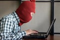 Masked hacker wearing a balaclava with laptop stealing importance data. Internet crime concept.