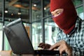 Masked hacker wearing a balaclava looking a laptop and stealing important information data. Network security and privacy crime con Royalty Free Stock Photo