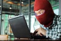 Masked hacker wearing a balaclava stealing data from laptop. Internet crime concept. Royalty Free Stock Photo