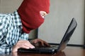 Masked hacker wearing a balaclava stealing information data with laptop. Internet crime concept. Royalty Free Stock Photo