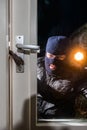 Masked intruder holding torch while trying to open window with c