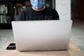 The masked man sat on the floor and worked at home using a laptop and holding a smartphone on a wooden table during the