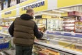 A masked man in a supermarket picks out convenience foods in the frozen food section. Back view. Moscow, Russia, 11-25-2020