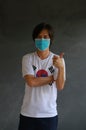 Masked man wearing South Korea flag color of shirt and cross one s arm with thumbs up on dark wall background