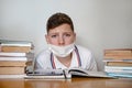 A masked teenager at home for textbooks with a tired look looks into the frame