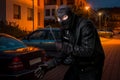 Masked thief in balaclava with crowbar wants to rob a car Royalty Free Stock Photo