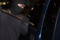 Masked thief with balaclava using crowbar to breaking into a car. Crime concept