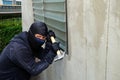 Masked thief using a hammer trying to break windows