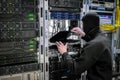 A masked thug closes a laptop in a server room. Hacker breaks into a computer in a data center.