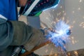Masked welder works in workshop and sparks fly. Close-up portrait. Industrial background. Authentic workflow.