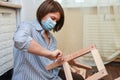 Masked woman is assembling wooden furniture with tools during quarantine isolation Royalty Free Stock Photo