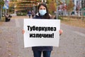 A masked woman holds a poster with text in Russian, translated from Russian - Tuberculosis is curable