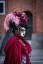 Masked woman in red dress with pink and purple featheres at Venetian carnaval