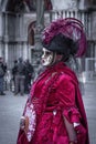 Masked woman in red dress with purple featheres on black hat and hand fan at Venetian carnaval Royalty Free Stock Photo