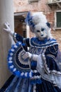 Masked woman wearing a decorative blue dress standing on next to an old stone column during Venice Carnival