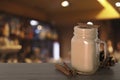 Mason jar with delicious eggnog, cinnamon sticks and cone on wooden table in bar, space for text