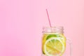 Mason jar glass of homemade lemonade with lemons, mint and red paper straw on pink background. Summer refreshing beverage Royalty Free Stock Photo