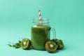 Mason jar with green smoothie and ingredients on mint background