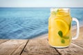 Mason jar with lemonade on table near sea, space for text
