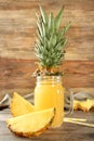 Mason jar of sweet juice with pineapple slices on wooden table