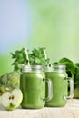 Mason jars of fresh green smoothie and ingredients on wooden table, space for text