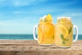 Mason jars with lemonade on table near sea, space for text