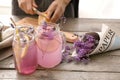 Mason jars with tasty beverage and young woman preparing lavender lemonade at table