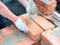 Mason in protective gloves is laying brick wall of a house construction using mortar, trowel and level line, string and spirit Royalty Free Stock Photo