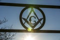 Masonic square and compass sign backlit against a blue sky with sunflare