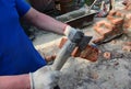 Masonry. How to hand cut a brick. A bricklayer is cutting a brick using a masonry tool, an axe while a brick wall, foundation